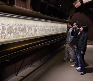 Un public équipé d'audioguide regarde la tapisserie.